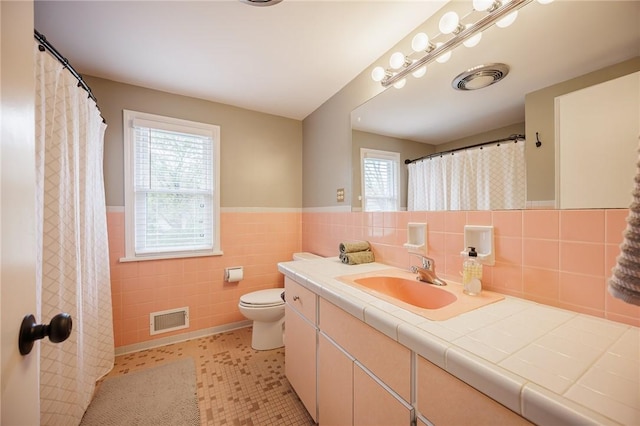 full bathroom featuring tile walls, wainscoting, toilet, and visible vents