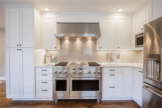 kitchen with decorative backsplash, dark wood-type flooring, wall chimney exhaust hood, white cabinetry, and stainless steel appliances