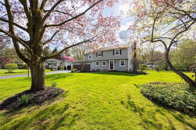 colonial home with a garage, a chimney, driveway, and a front lawn