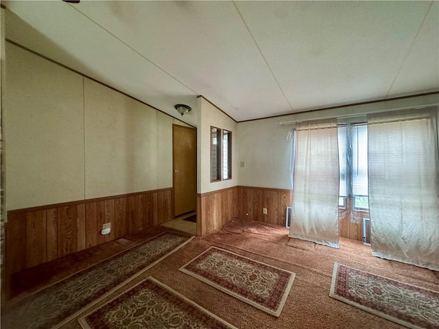 unfurnished room featuring carpet floors, wood walls, lofted ceiling, and a wainscoted wall