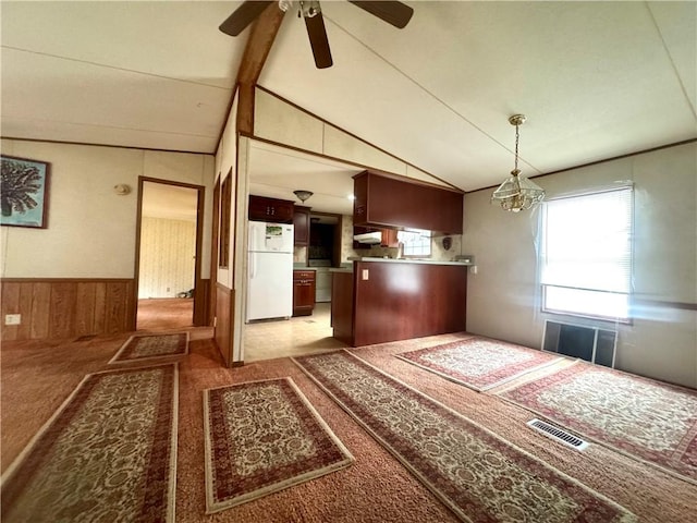 kitchen featuring wooden walls, lofted ceiling with beams, ceiling fan with notable chandelier, freestanding refrigerator, and visible vents