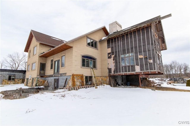 snow covered house featuring a chimney, a sunroom, and stone siding