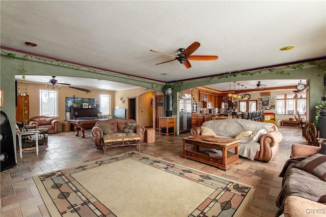 living area with stone tile flooring, arched walkways, ceiling fan, and a textured ceiling