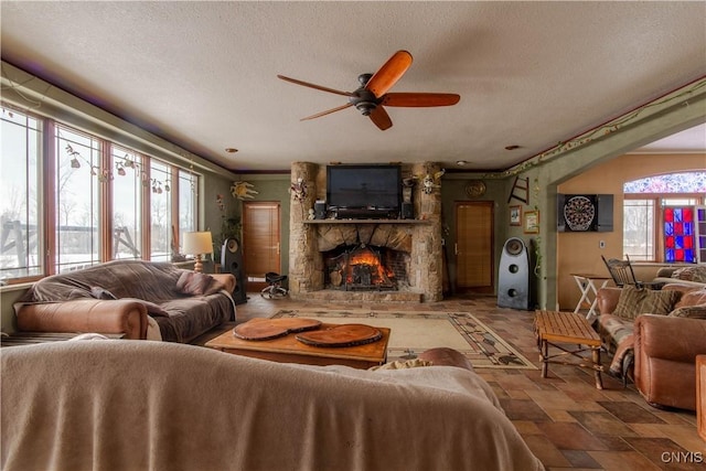 living room with a stone fireplace, stone finish flooring, a textured ceiling, and ceiling fan