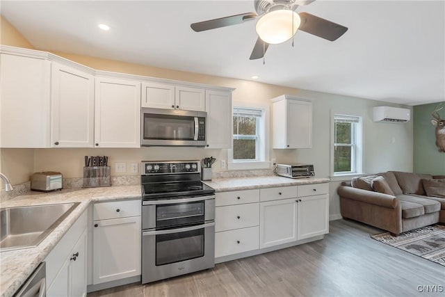 216 Harry Bryant Rd, Amboy, NY 13493 - kitchen featuring stainless steel appliances, a sink, an AC wall unit, white cabinetry, and light wood-style floors