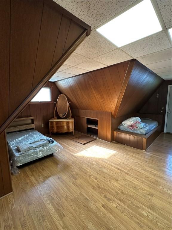 unfurnished bedroom featuring wooden walls, vaulted ceiling, and wood finished floors