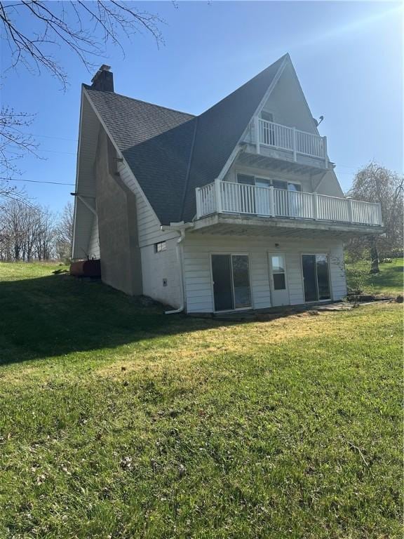 rear view of house with a lawn, a balcony, and a chimney
