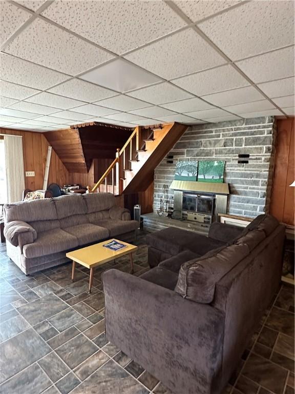 living area with wooden walls, stone finish flooring, a paneled ceiling, and stairway