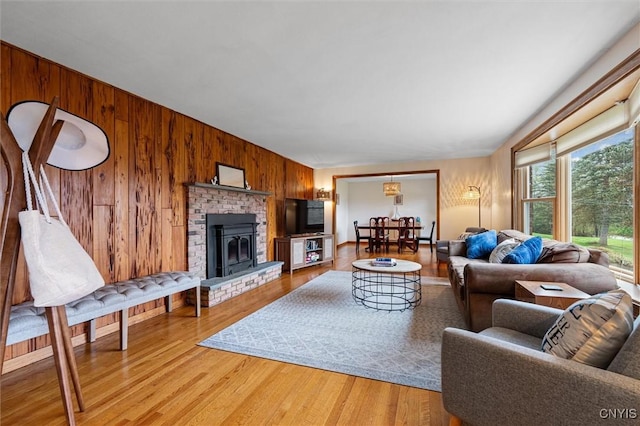 living area with wood walls, light wood finished floors, a brick fireplace, and baseboards