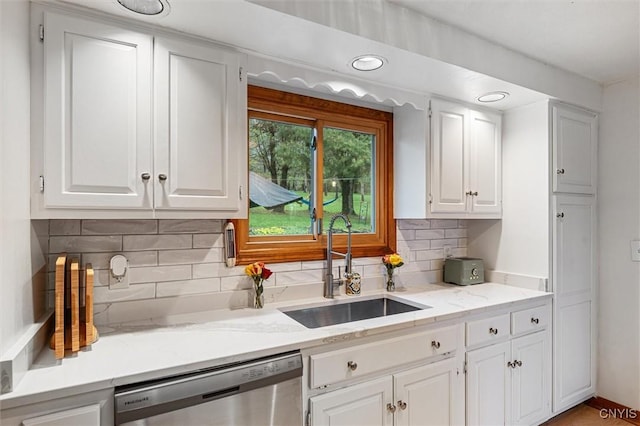kitchen with stainless steel dishwasher, a sink, white cabinetry, backsplash, and light stone countertops
