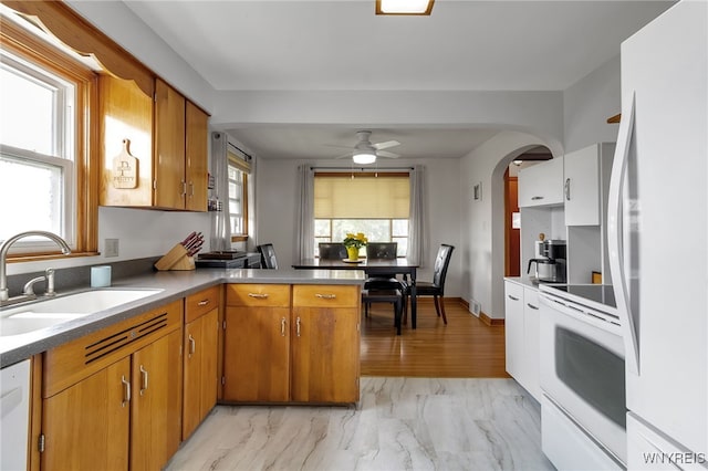 kitchen with brown cabinets, a sink, white appliances, arched walkways, and a peninsula