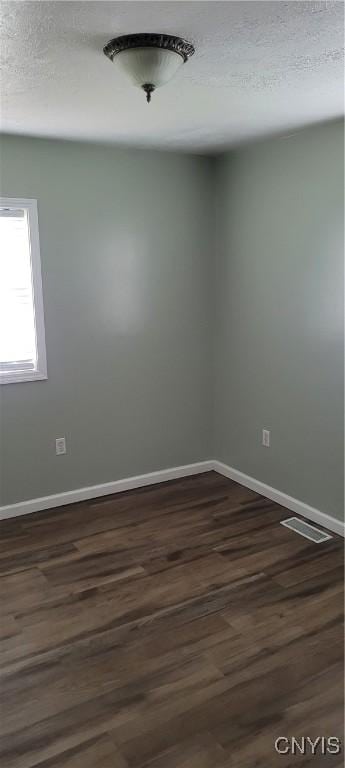 unfurnished room featuring baseboards, visible vents, a textured ceiling, and dark wood-type flooring
