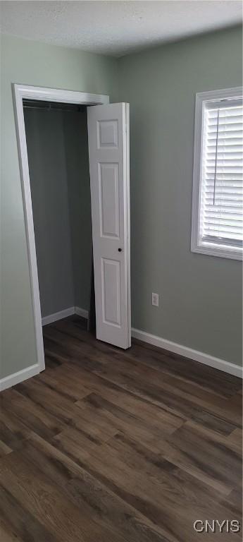 unfurnished bedroom featuring dark wood-style flooring, baseboards, and a closet