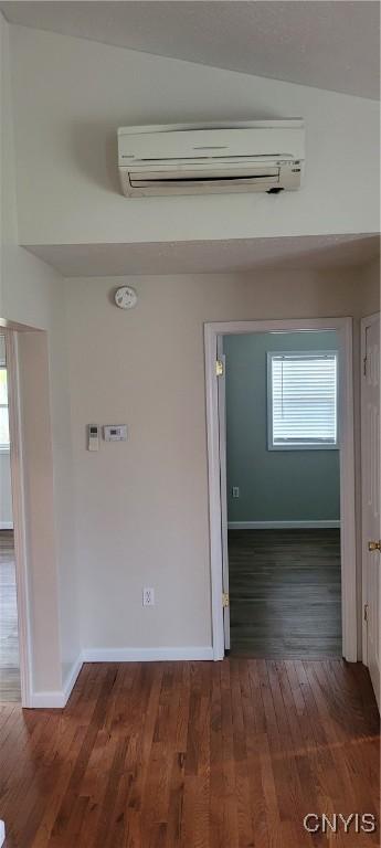 hall featuring baseboards, a wall unit AC, and wood finished floors