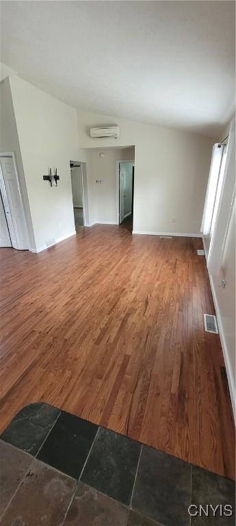 206 Oak St, Fulton, NY 13069 - unfurnished living room with wood finished floors, a wall mounted air conditioner, visible vents, baseboards, and vaulted ceiling