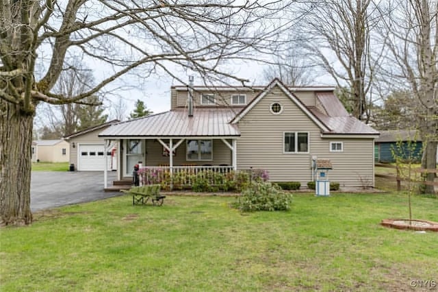 view of front facade with covered porch, driveway, metal roof, a garage, and a front lawn