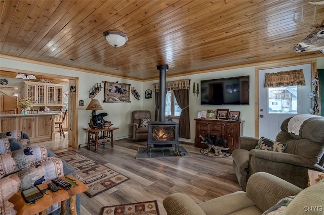 living room featuring light wood-type flooring, a wood stove, wooden ceiling, and ornamental molding