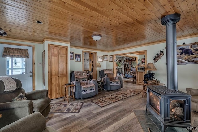 living area with ornamental molding, wood ceiling, a wood stove, and wood finished floors