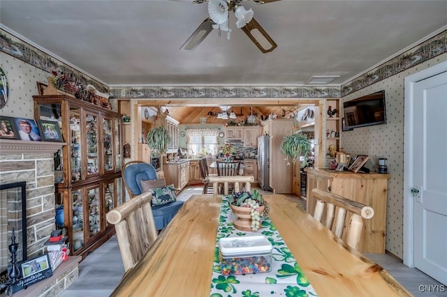 dining space with crown molding, ceiling fan, a fireplace, and wallpapered walls