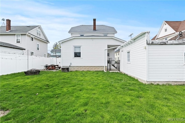 rear view of house with a fenced backyard, a chimney, a yard, and a fire pit