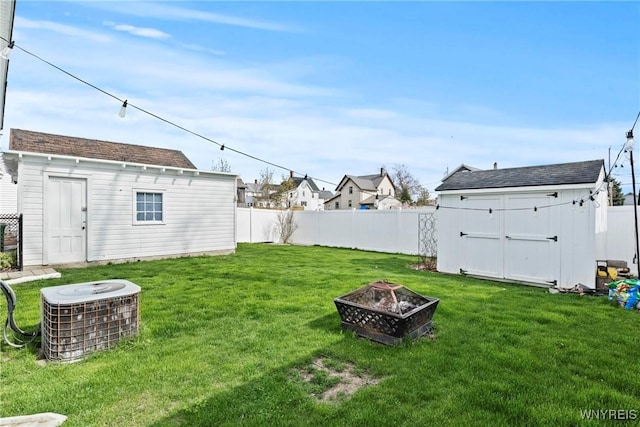 view of yard featuring an outdoor structure, a fenced backyard, an outdoor fire pit, and central AC