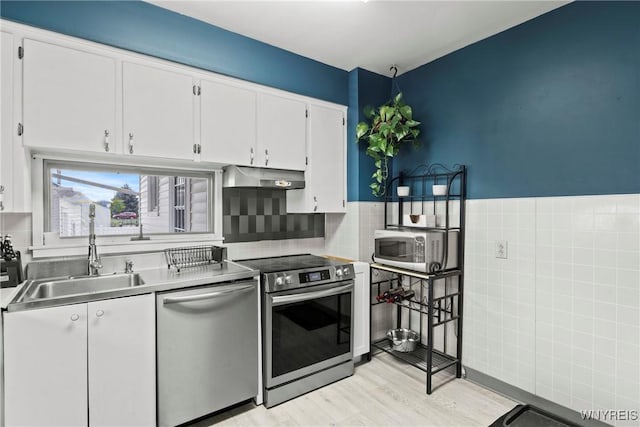 kitchen featuring appliances with stainless steel finishes, a sink, white cabinets, under cabinet range hood, and light wood-style flooring