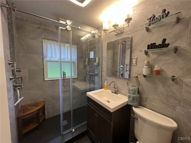 full bathroom featuring vanity, toilet, tile walls, a textured ceiling, and a stall shower