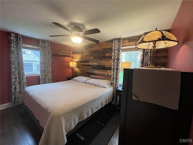 bedroom featuring wooden walls, ceiling fan, baseboards, and wood finished floors