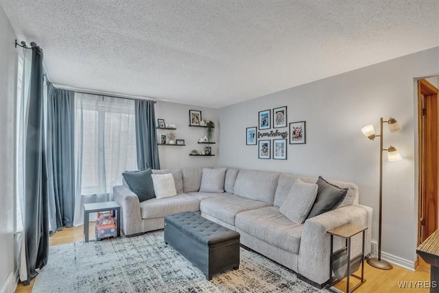 living area with light wood-type flooring, a textured ceiling, and baseboards