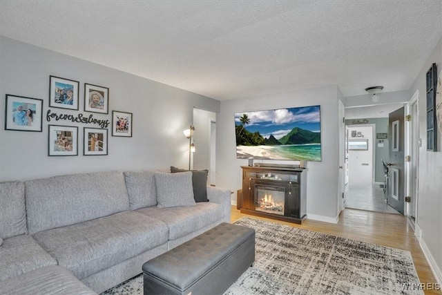living area featuring a glass covered fireplace, baseboards, light wood-type flooring, and a textured ceiling