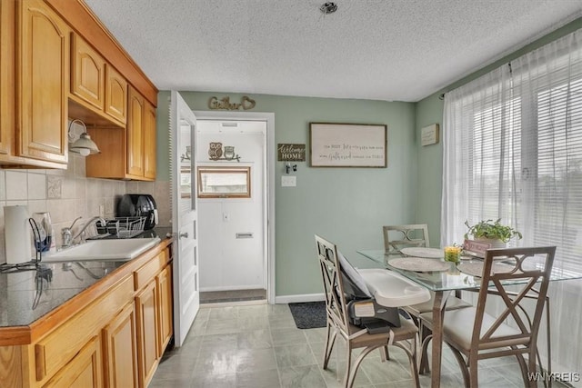 kitchen featuring a sink, a textured ceiling, tile countertops, baseboards, and tasteful backsplash