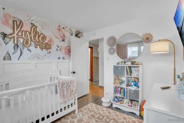 bedroom featuring wainscoting, a crib, and wood finished floors