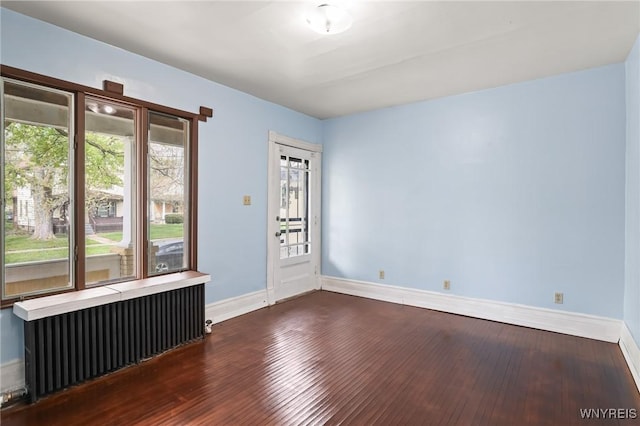 empty room with baseboards, wood finished floors, and radiator