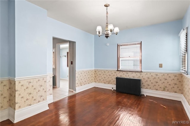 spare room featuring radiator heating unit, hardwood / wood-style flooring, wallpapered walls, and a healthy amount of sunlight