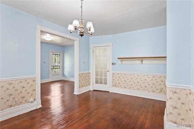 unfurnished dining area with wallpapered walls, a notable chandelier, wainscoting, and wood finished floors