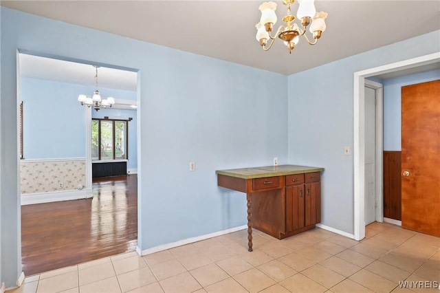 unfurnished dining area featuring light tile patterned floors, baseboards, and a notable chandelier
