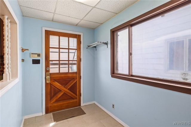 doorway to outside featuring baseboards, a drop ceiling, and light tile patterned floors