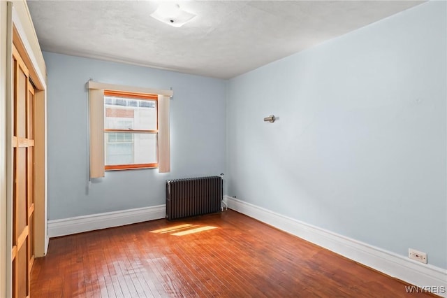 spare room with radiator heating unit, baseboards, and hardwood / wood-style flooring