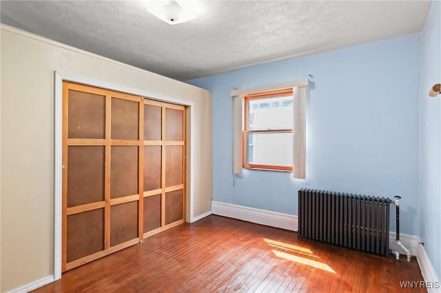 unfurnished bedroom featuring a closet, baseboards, radiator heating unit, and hardwood / wood-style floors