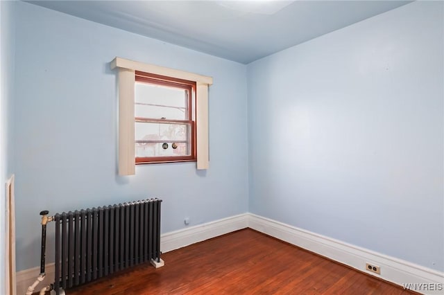 spare room with wood finished floors, baseboards, and radiator heating unit