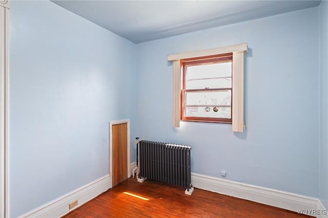 empty room with baseboards, wood finished floors, and radiator