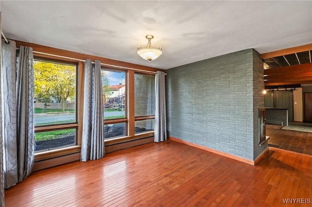 spare room featuring wood-type flooring, brick wall, and baseboards