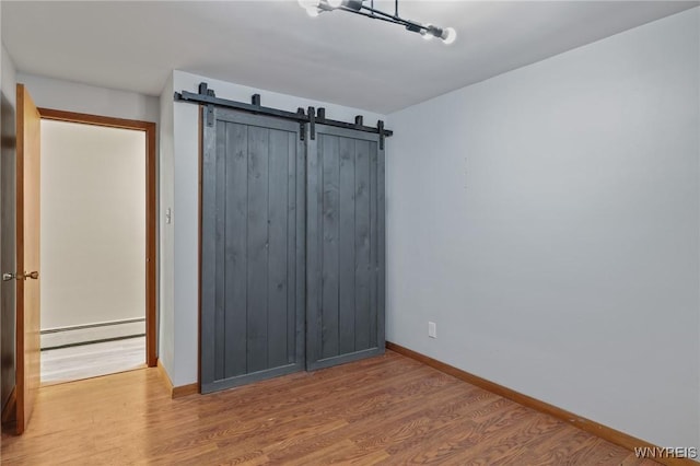 unfurnished bedroom with wood finished floors, a barn door, baseboards, and a baseboard heating unit