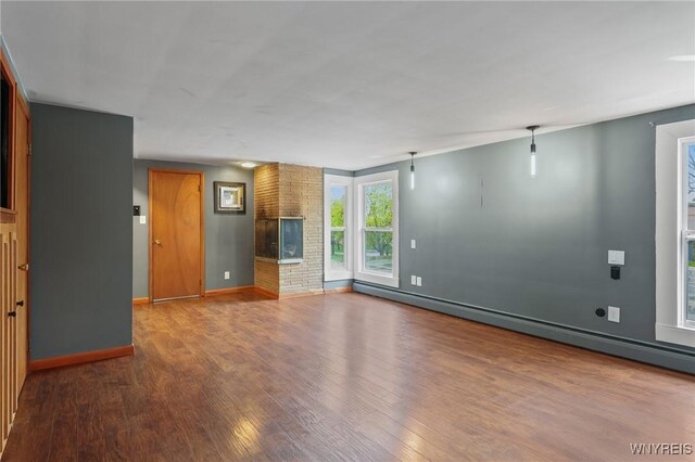 unfurnished living room featuring baseboards, a baseboard heating unit, and wood finished floors