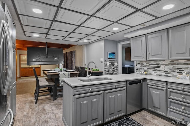 kitchen featuring appliances with stainless steel finishes, a sink, light wood-style flooring, a peninsula, and gray cabinetry