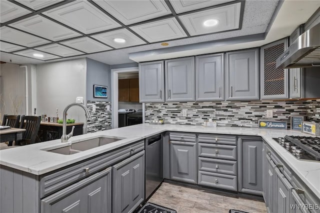 kitchen featuring wall chimney range hood, a sink, stainless steel appliances, a peninsula, and gray cabinetry