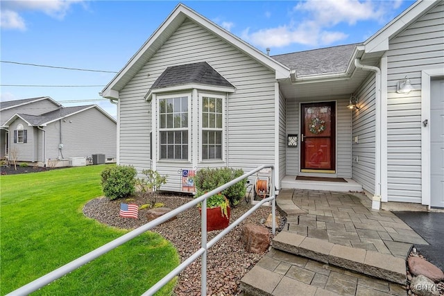 view of exterior entry featuring roof with shingles, central AC unit, and a yard