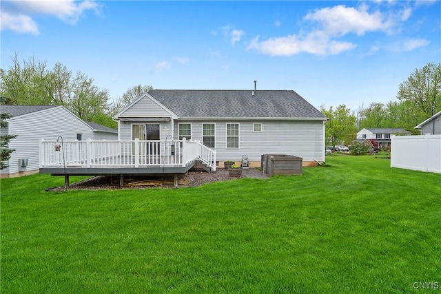 back of property with a lawn, roof with shingles, fence, and a deck