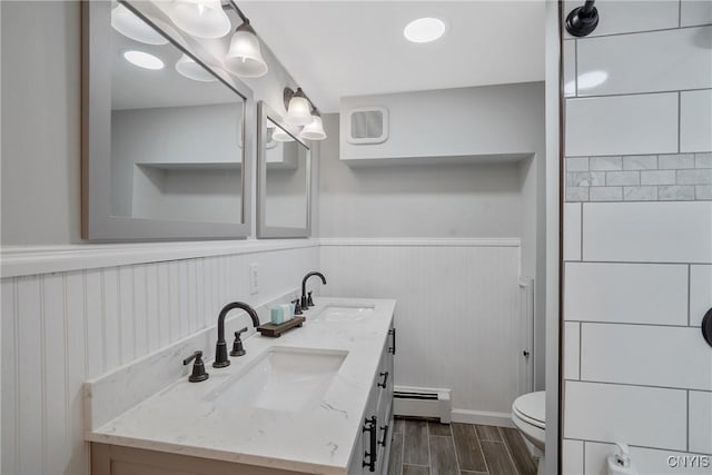 full bathroom with a sink, wainscoting, a baseboard heating unit, and wood finished floors
