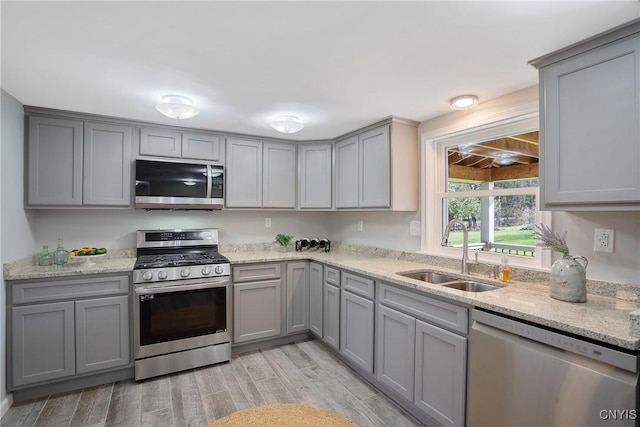 kitchen featuring a sink, appliances with stainless steel finishes, gray cabinetry, and light stone counters